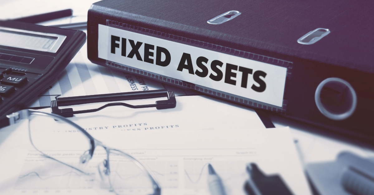 A binder labeled "Fixed Assets" sits on a desk with documents, a calculator, eyeglasses, and a clipboard—tools essential for managing fixed assets and tracking right of use fixed assets in 2024.