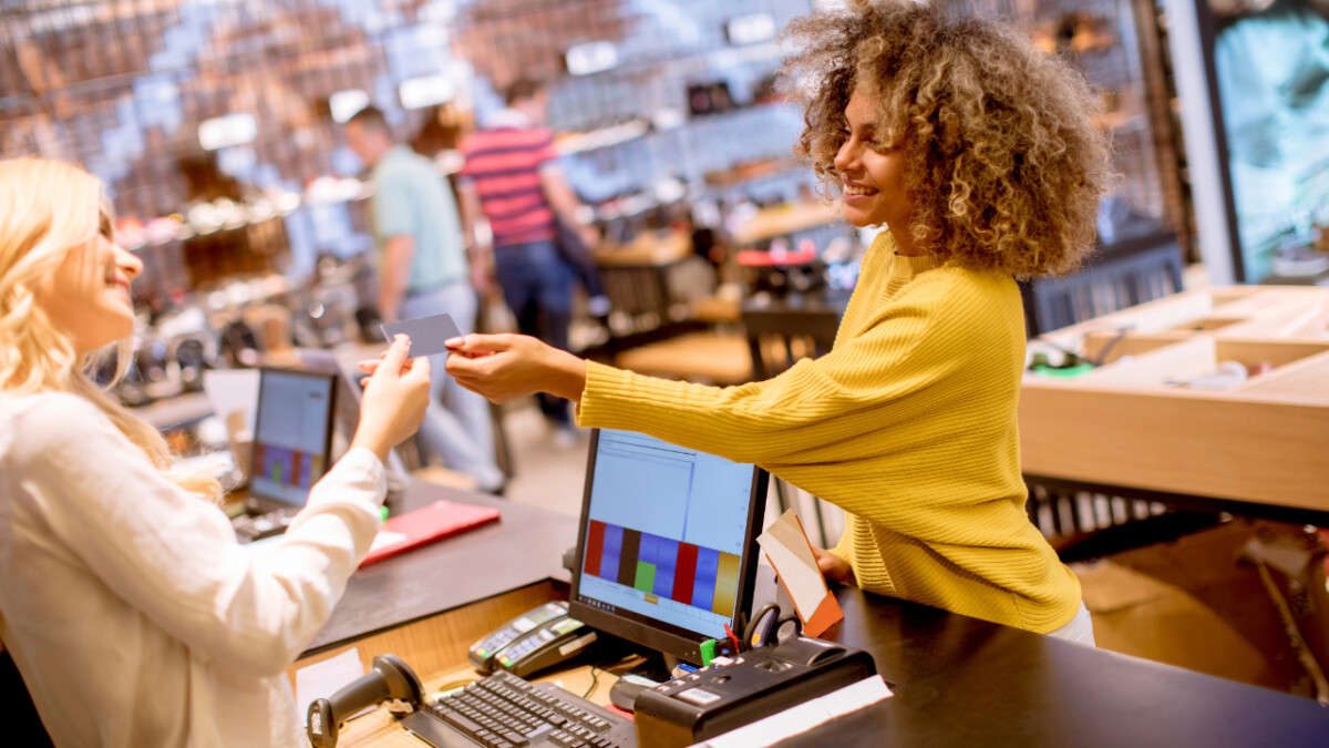 A smiling cashier in a yellow sweater hands a payment card to a customer at a retail store checkout counter, showcasing one of the best shop ideas for 2024.