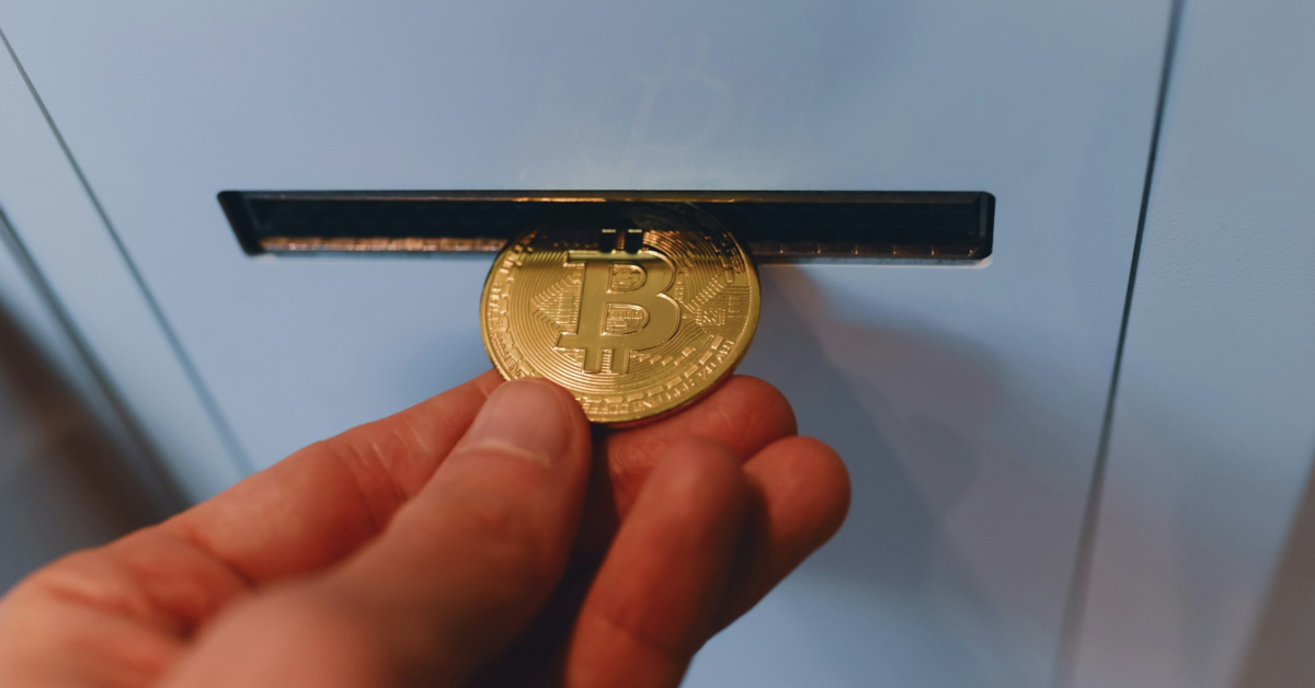A hand inserts a physical Bitcoin token into a narrow slot on a light blue surface, symbolizing how ecommerce websites can incorporate crypto payments seamlessly.