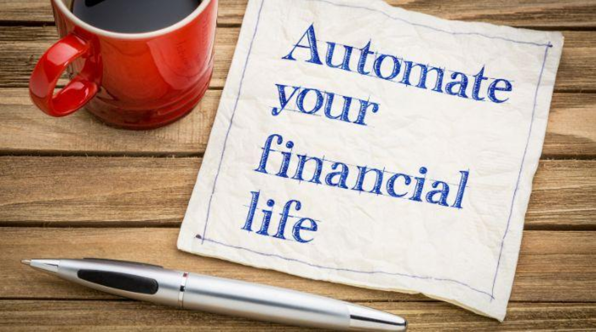 A red coffee mug, a pen, and a napkin with the printed words "Automate your financial life" on a wooden surface highlight the benefits of automating your savings.