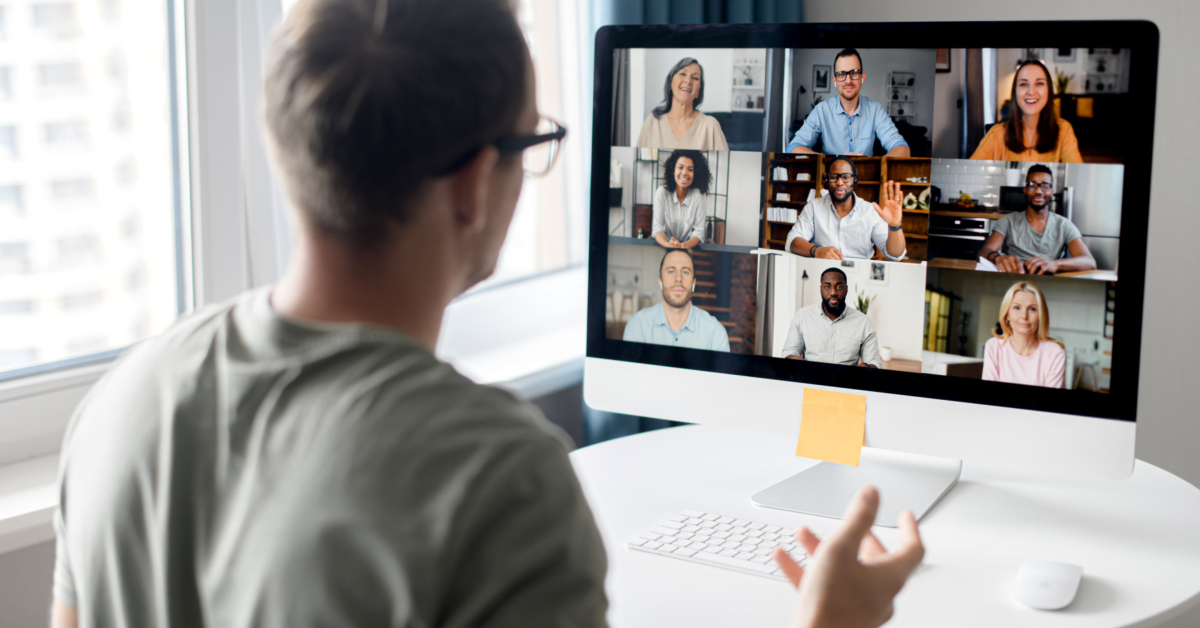 A person sits at a desk, participating in a video conference with eight people on a computer screen, using virtual training software for an interactive learning experience.