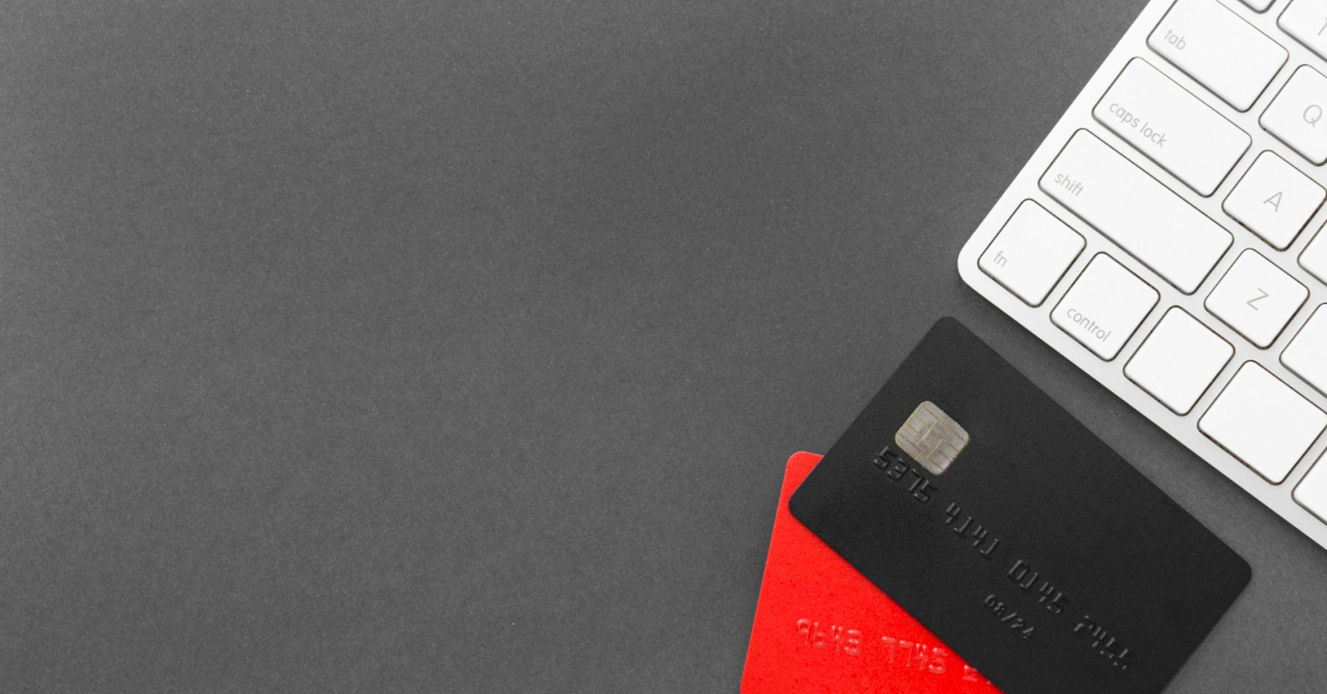 A white computer keyboard sits next to a black credit card and a red credit card on a dark gray surface, perfect for businesses or e-commerce setups exploring efficient credit card processors.