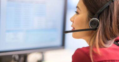 Woman wearing a headset sits at a desk and looks at a computer screen, providing customer support solutions for retailers, possibly in an e-commerce outsourcing Philippines environment.
