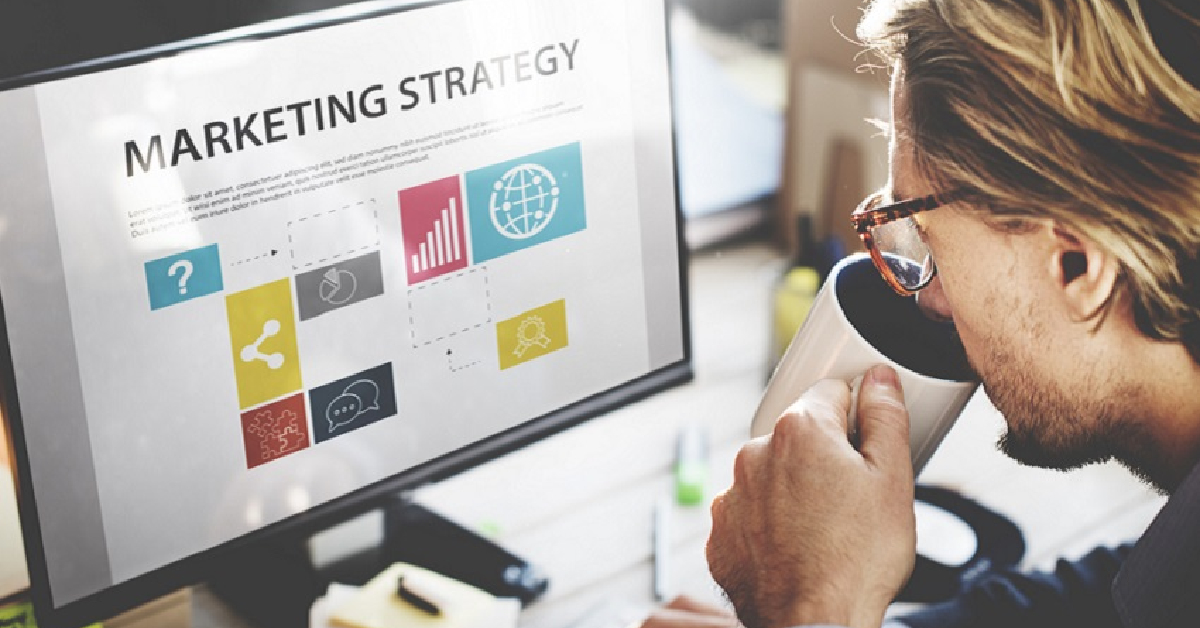 A person drinks from a mug while looking at a computer monitor displaying a digital marketing strategy diagram with icons and graphs—perfect inspiration to get started on your small business plans.