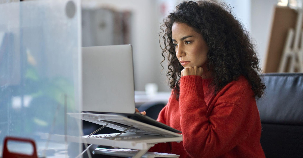 A woman in a red sweater sits at a desk in Mexico, looking intently at a laptop screen—perhaps exploring Retail Customer Support Outsourcing solutions for Ecommerce businesses.