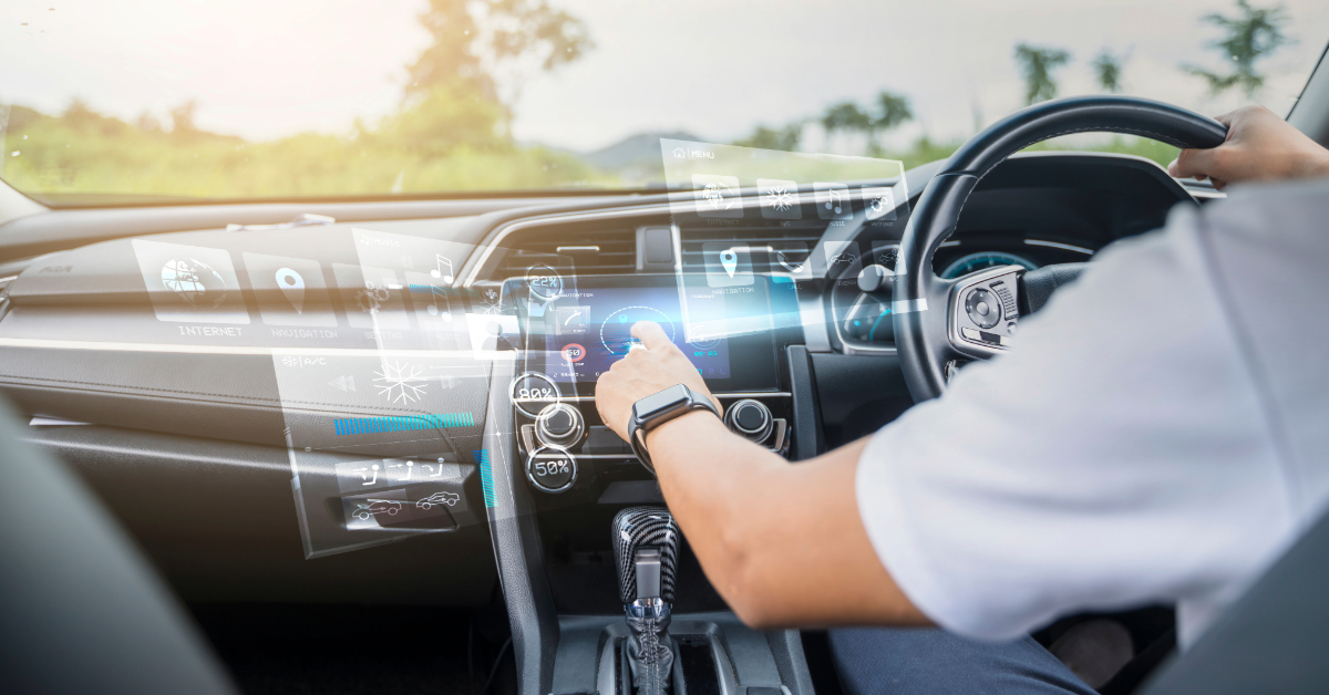 A person interacts with a transparent touchscreen interface while driving a modern car, displaying various digital controls and information holographically above the dashboard for smarter driving and enhanced road safety.