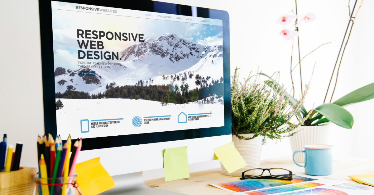 A desktop computer displays a "Responsive Web Design" webpage. The workspace, featuring essential elements like pens, sticky notes, a notebook, and a potted orchid, sits on a wooden desk—perfect for web design inspiration.